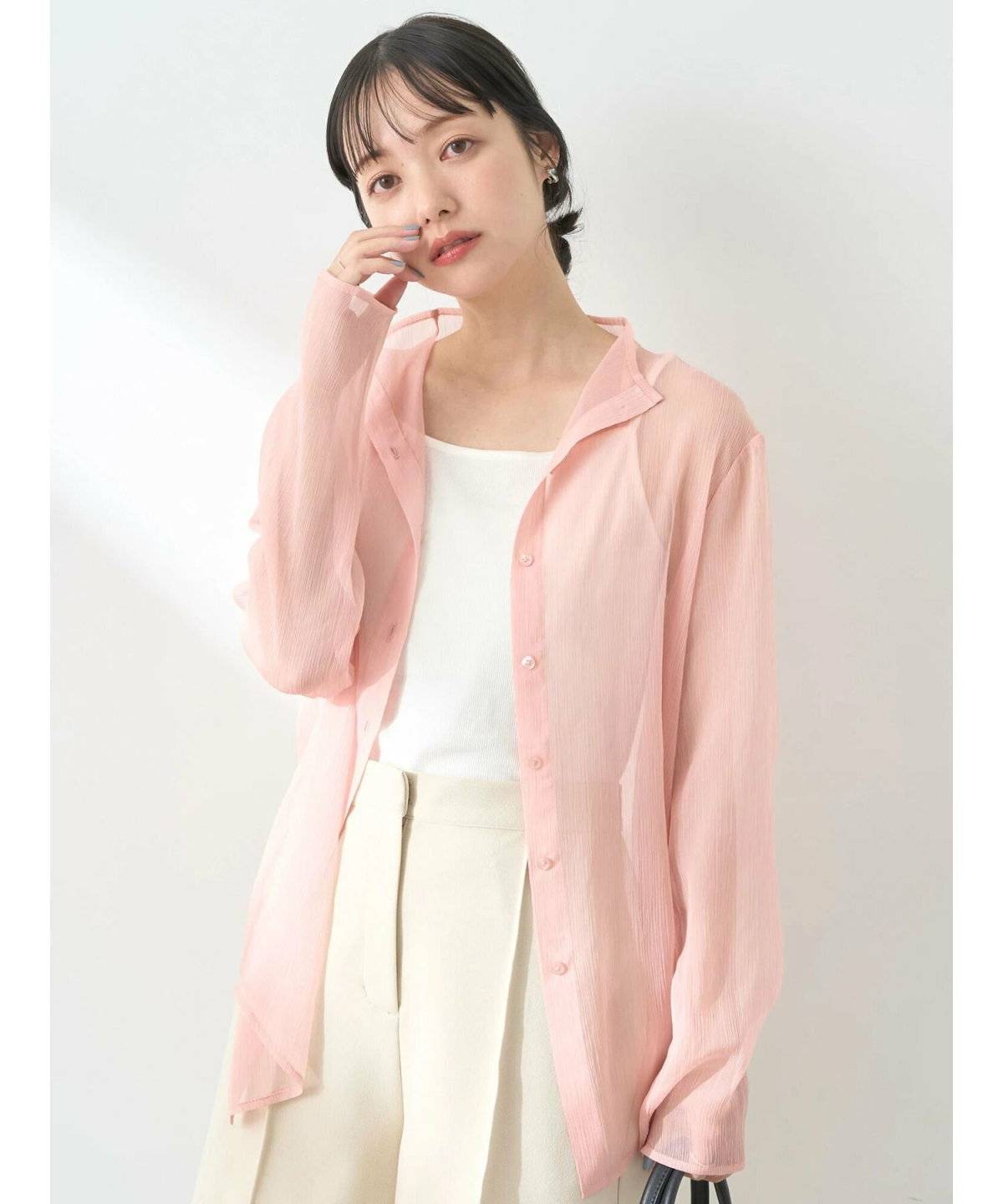 ホワイトコーデにピンクのシアーシャツを羽織った女性