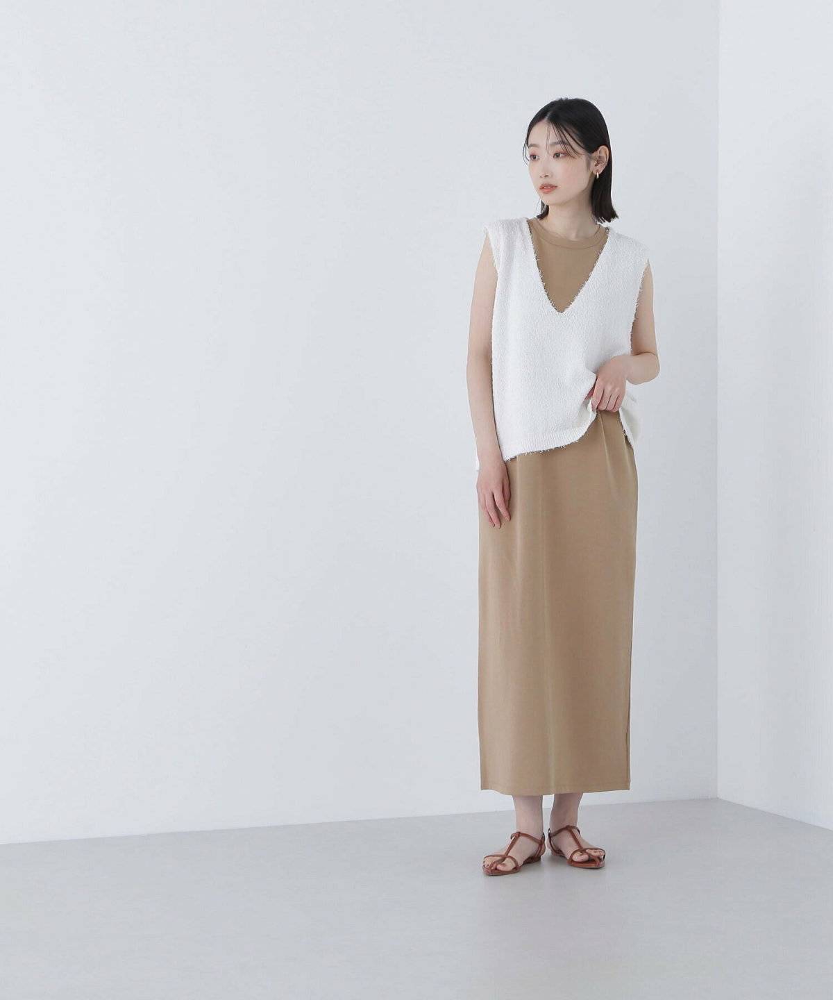 ベージュのワンピースにホワイトのベストを重ねた女性