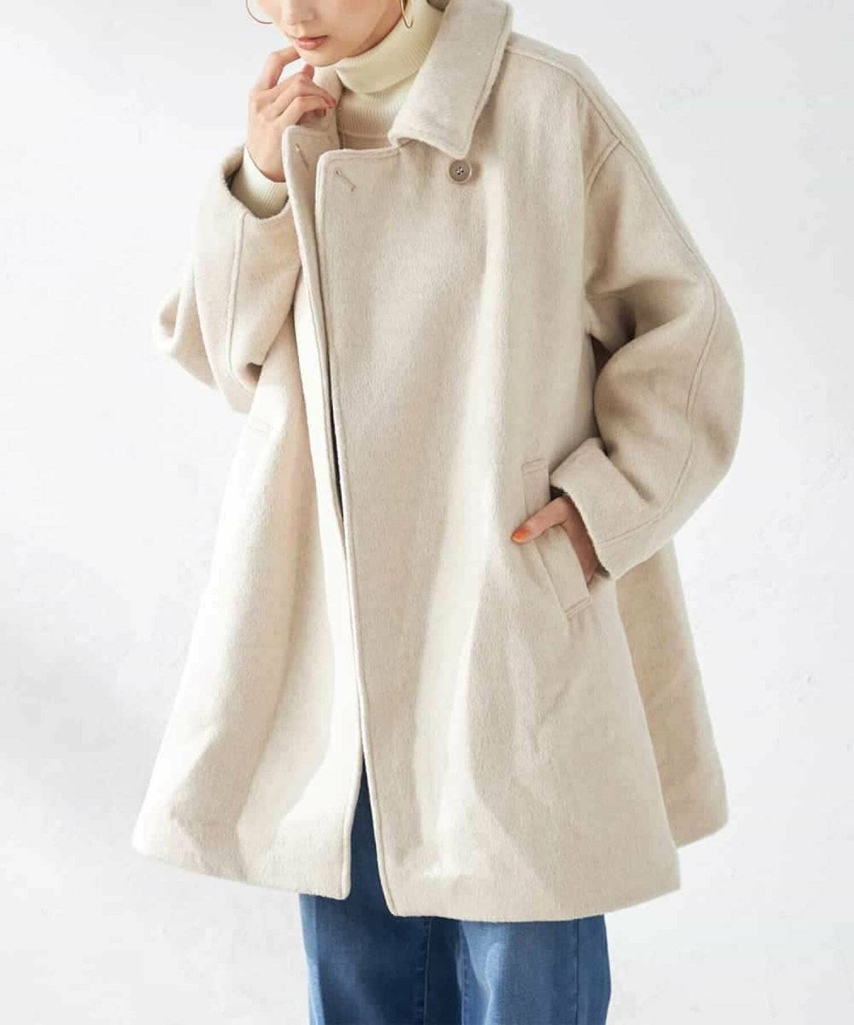 白ニットにデニムを合わせてベージュのジャケットを羽織った女性