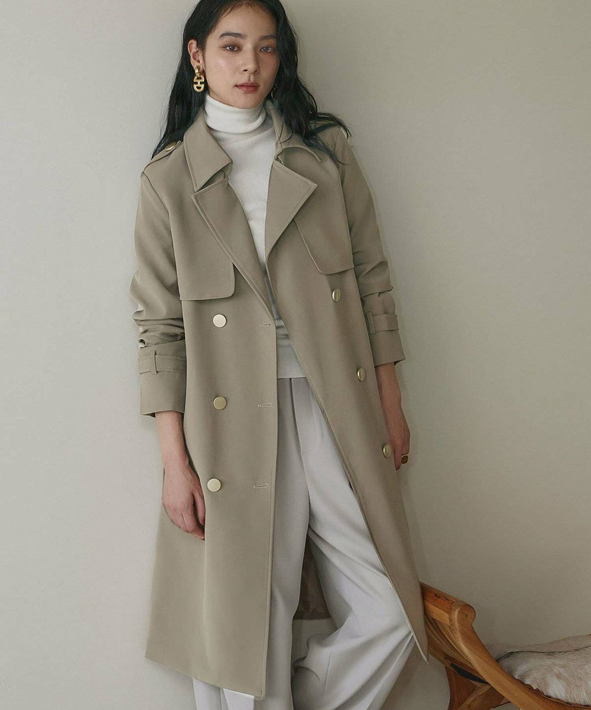 グリーンのロングトレンチコートに白パンツを合わせた女性
