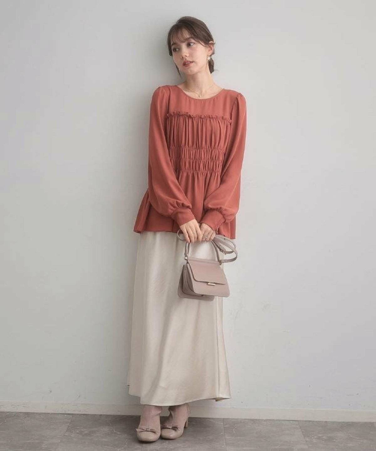 オレンジのブラウスに白スカートを合わせた女性