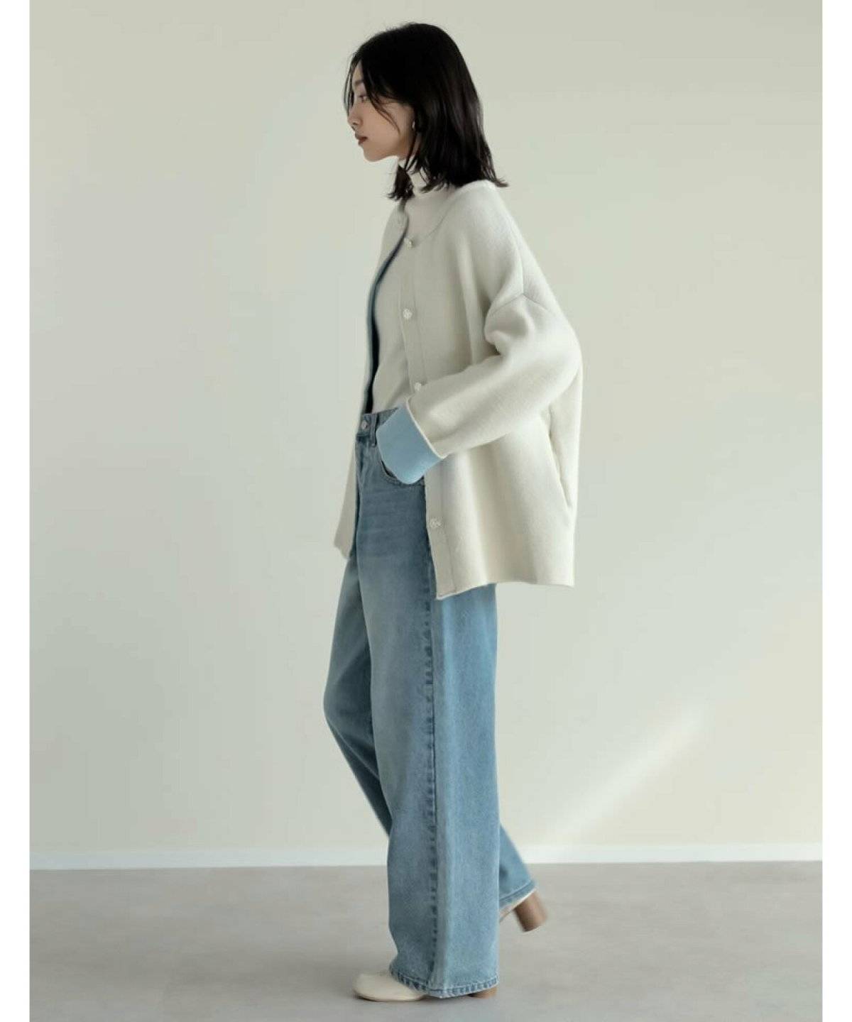 白のニットコートにグレーのデニムを合わせた女性