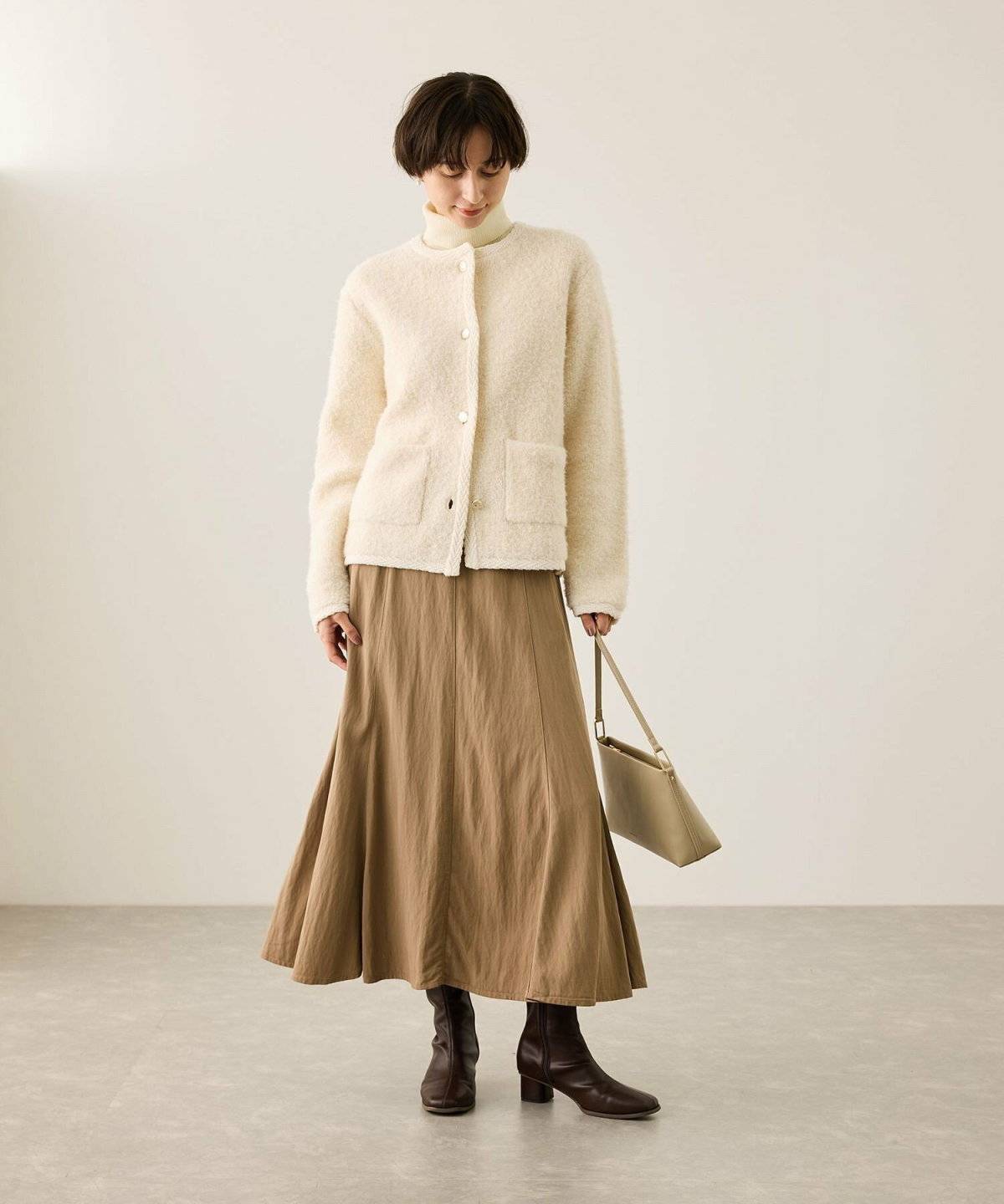 ベージュのカーディガンにブラウンのスカートを合わせた女性