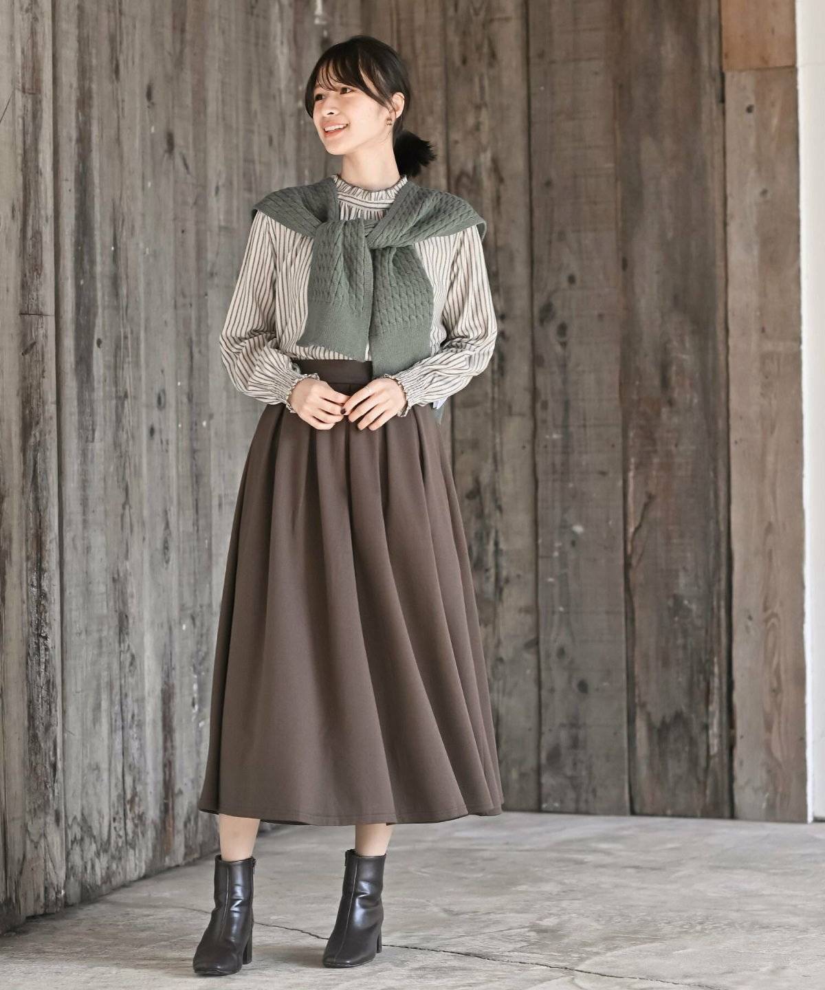 ベージュのカーディガンにブラウンのスカートを合わせた女性