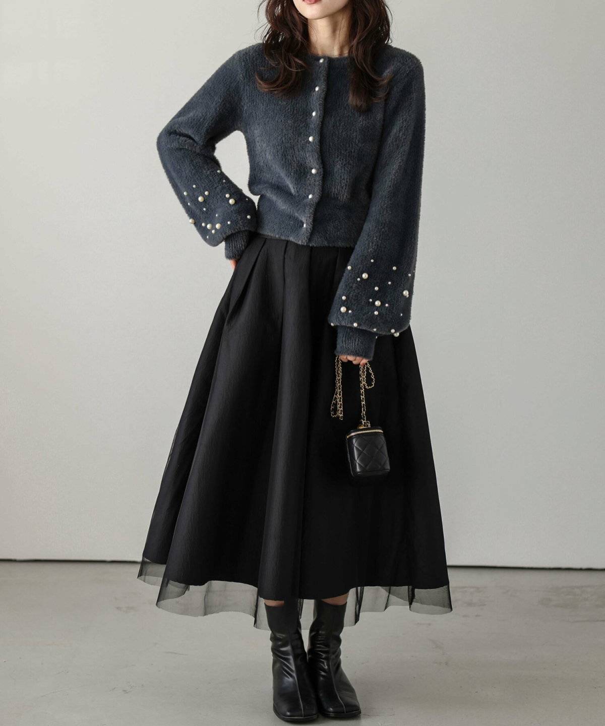 グレーのカーディガンに黒スカートを合わせた女性