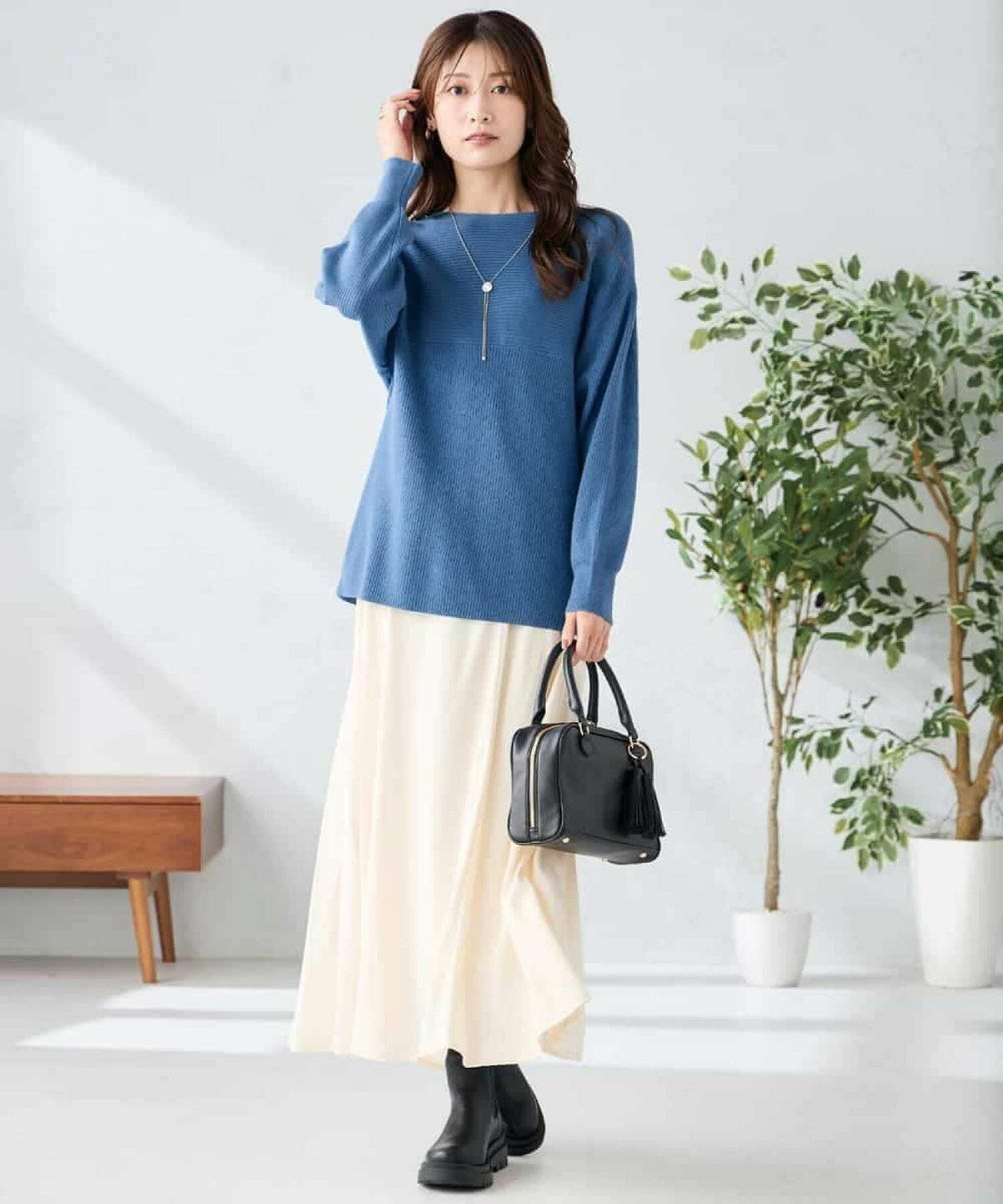 ベージュのワンピースの上にブルーのニットを重ねた女性