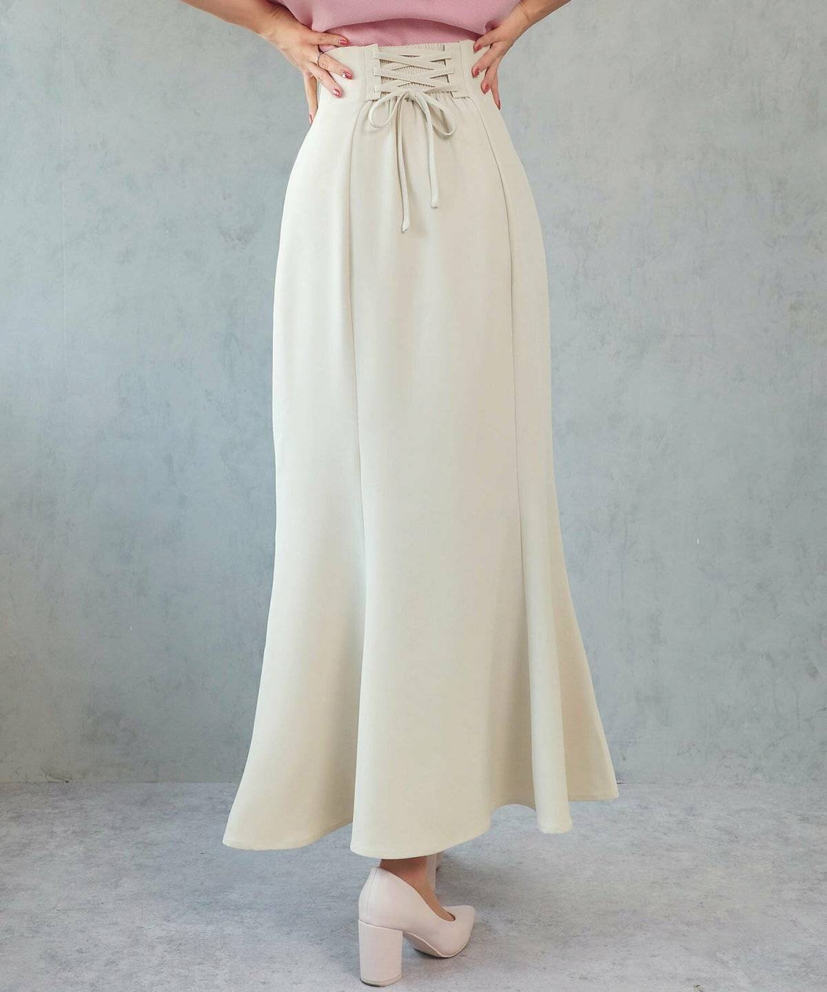 ピンクのトップスにホワイトのスカートを合わせた女性