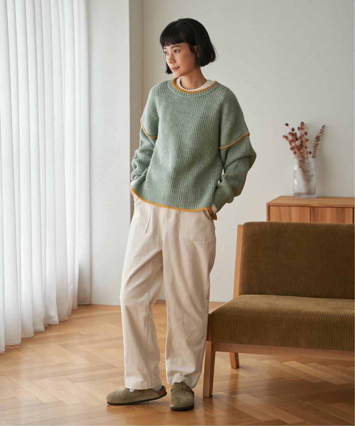 ミントグリーンのニットに白パンツを合わせた女性