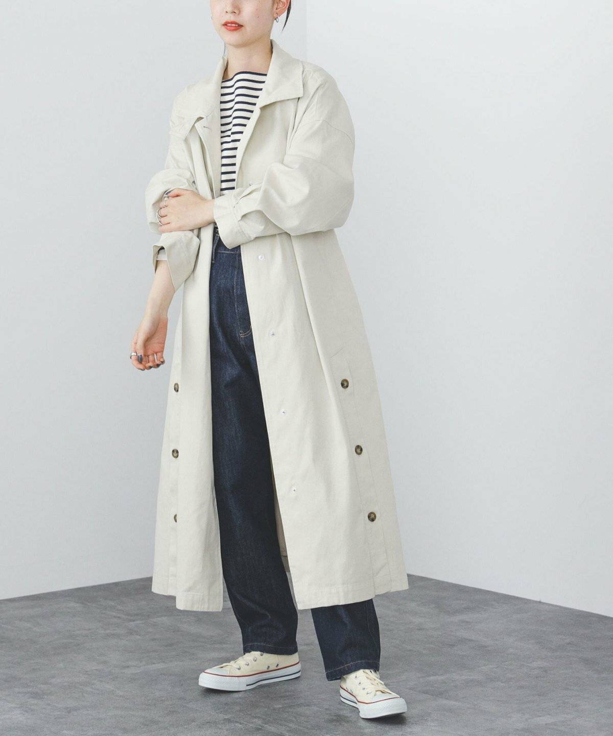 ボーダー柄トップスにパンツを合わせてベージュのコートを羽織った女性