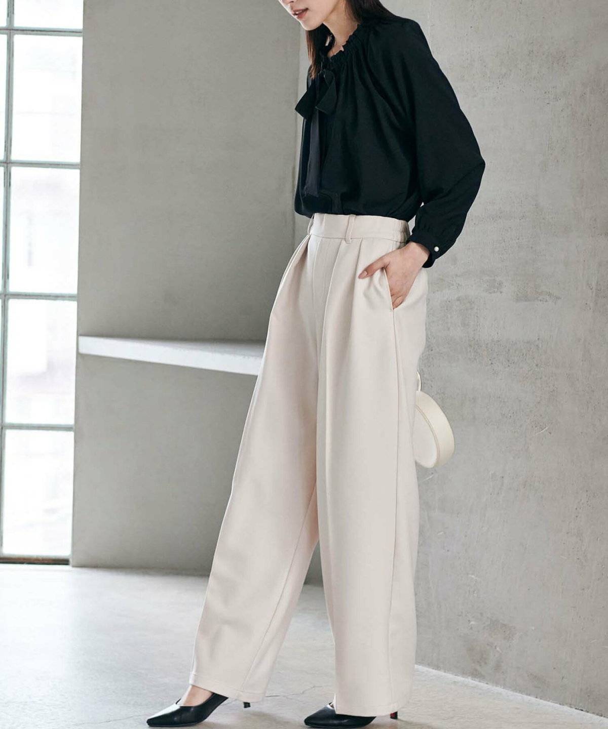 黒ブラウスにベージュのパンツを合わせた女性