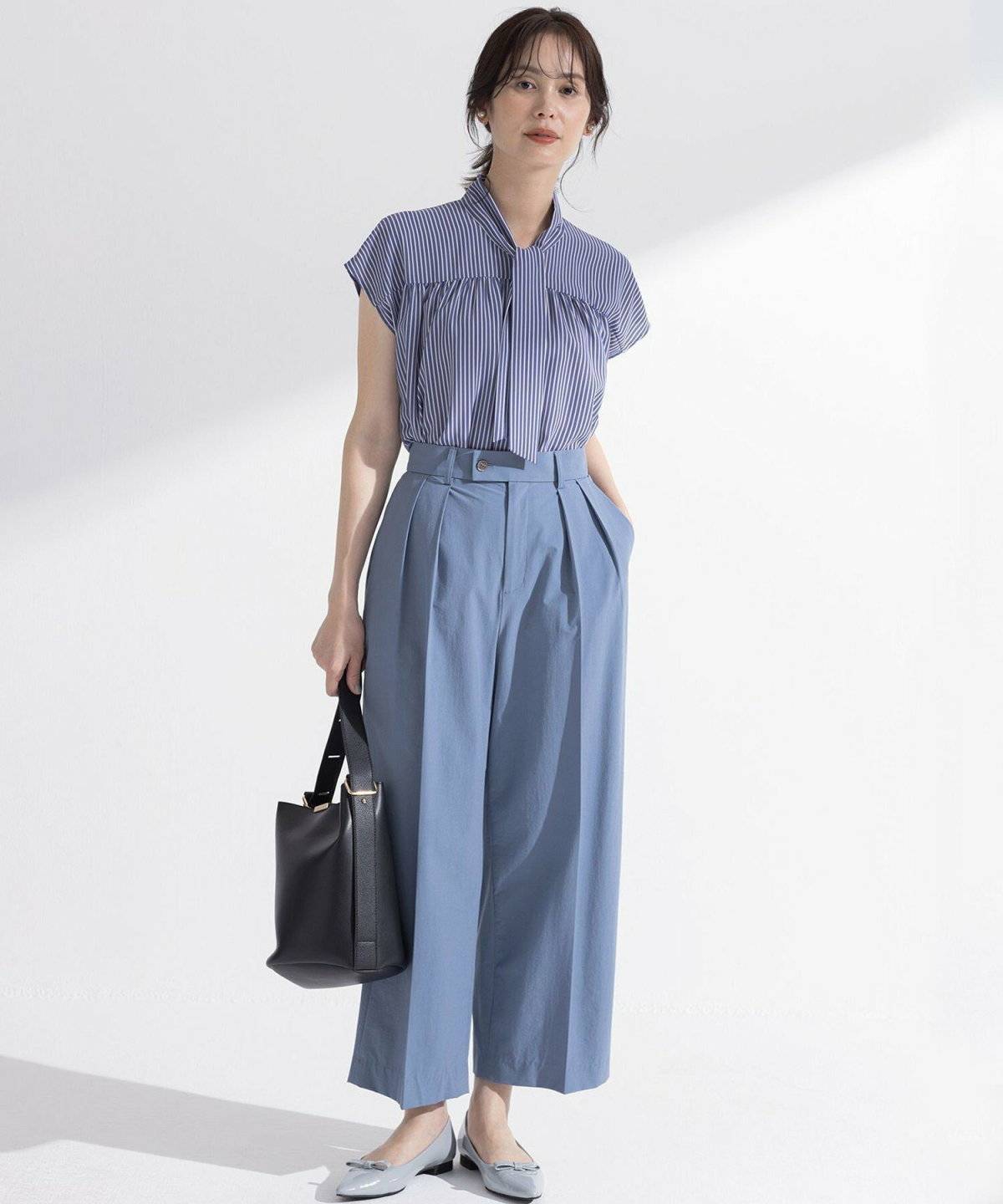 ブルーのブラウスに黒パンツを合わせた女性