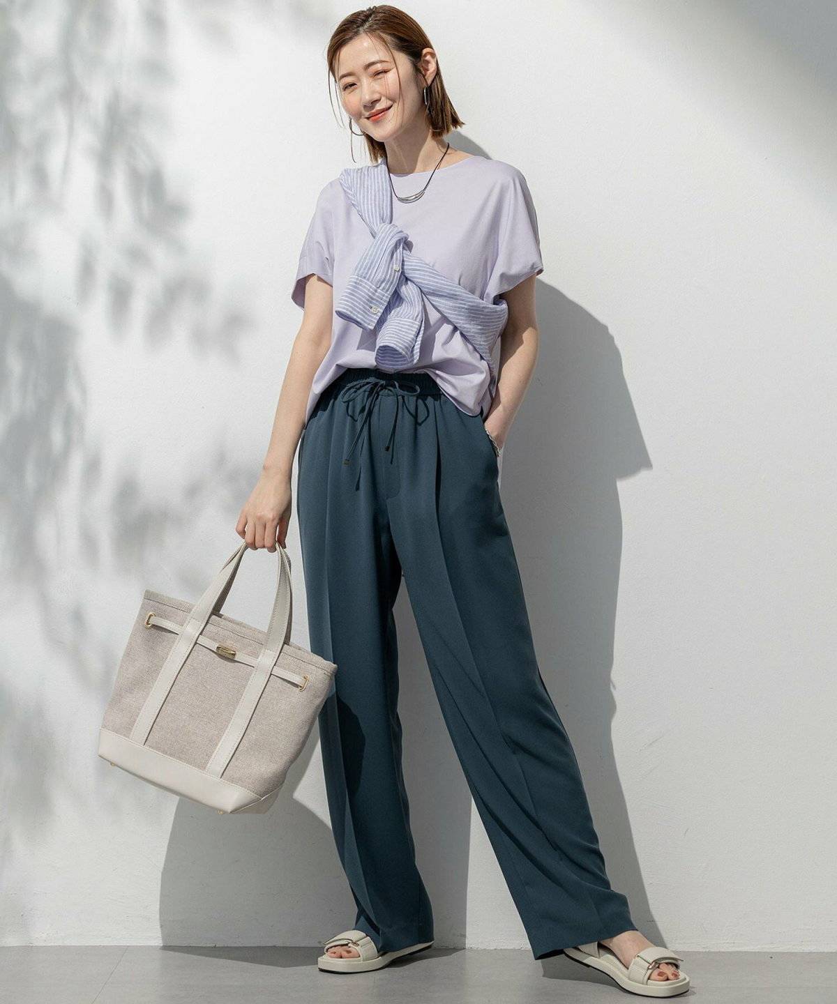 ラベンダーのストライプシャツ✕黒のテーパードパンツの女性