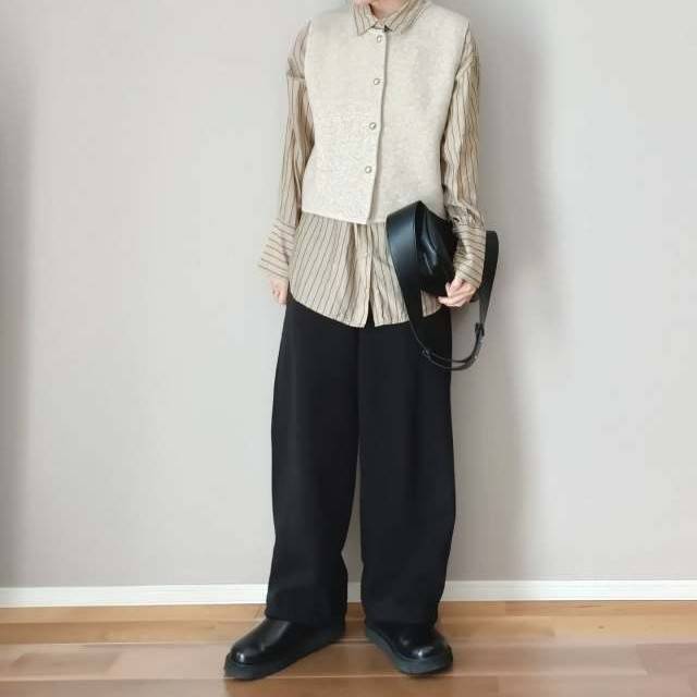 ストライプ柄のシャツにベストを重ね着して黒パンツを穿いた女性