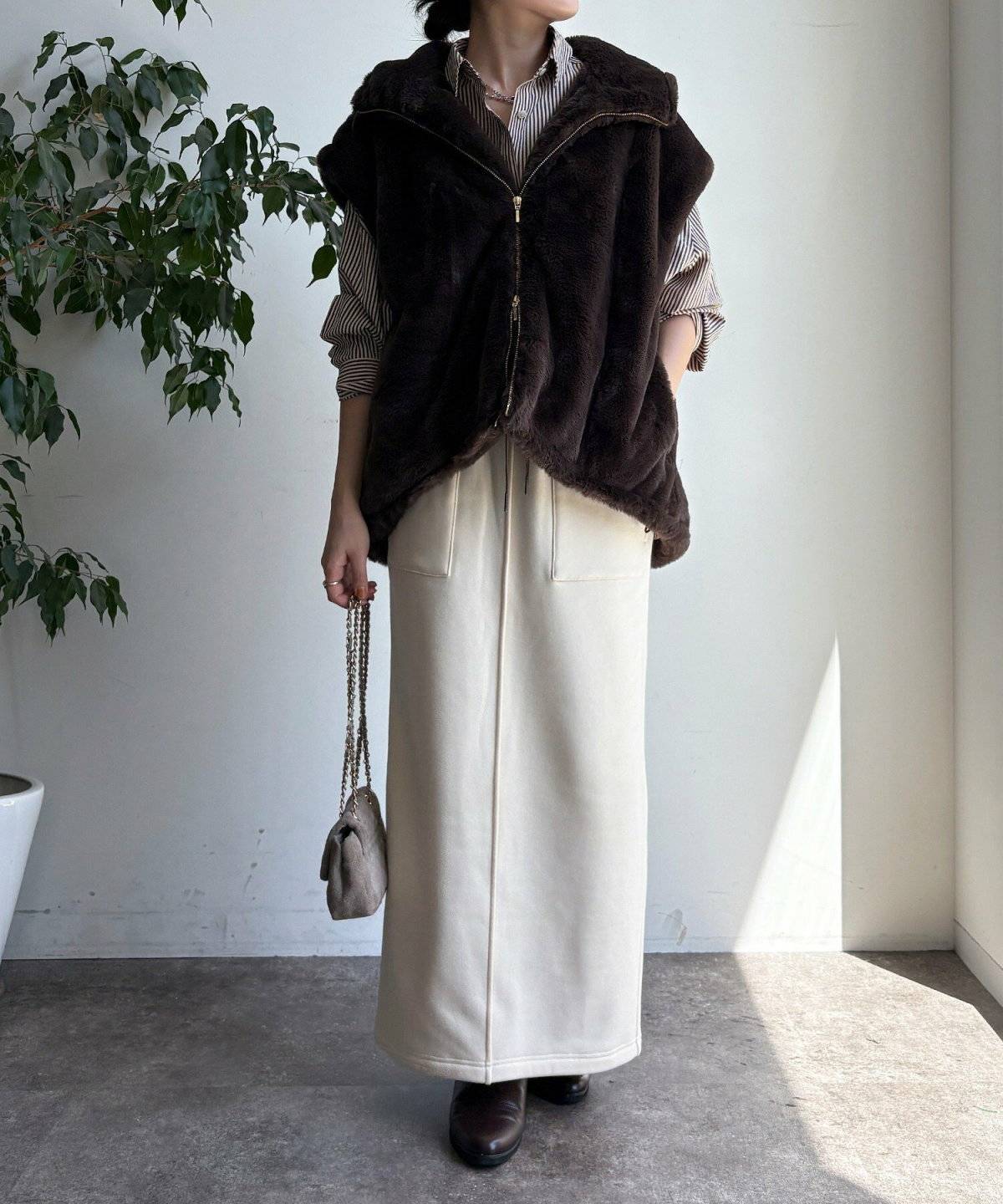 ホワイトコーデにブラウンのファーベストを重ねた女性