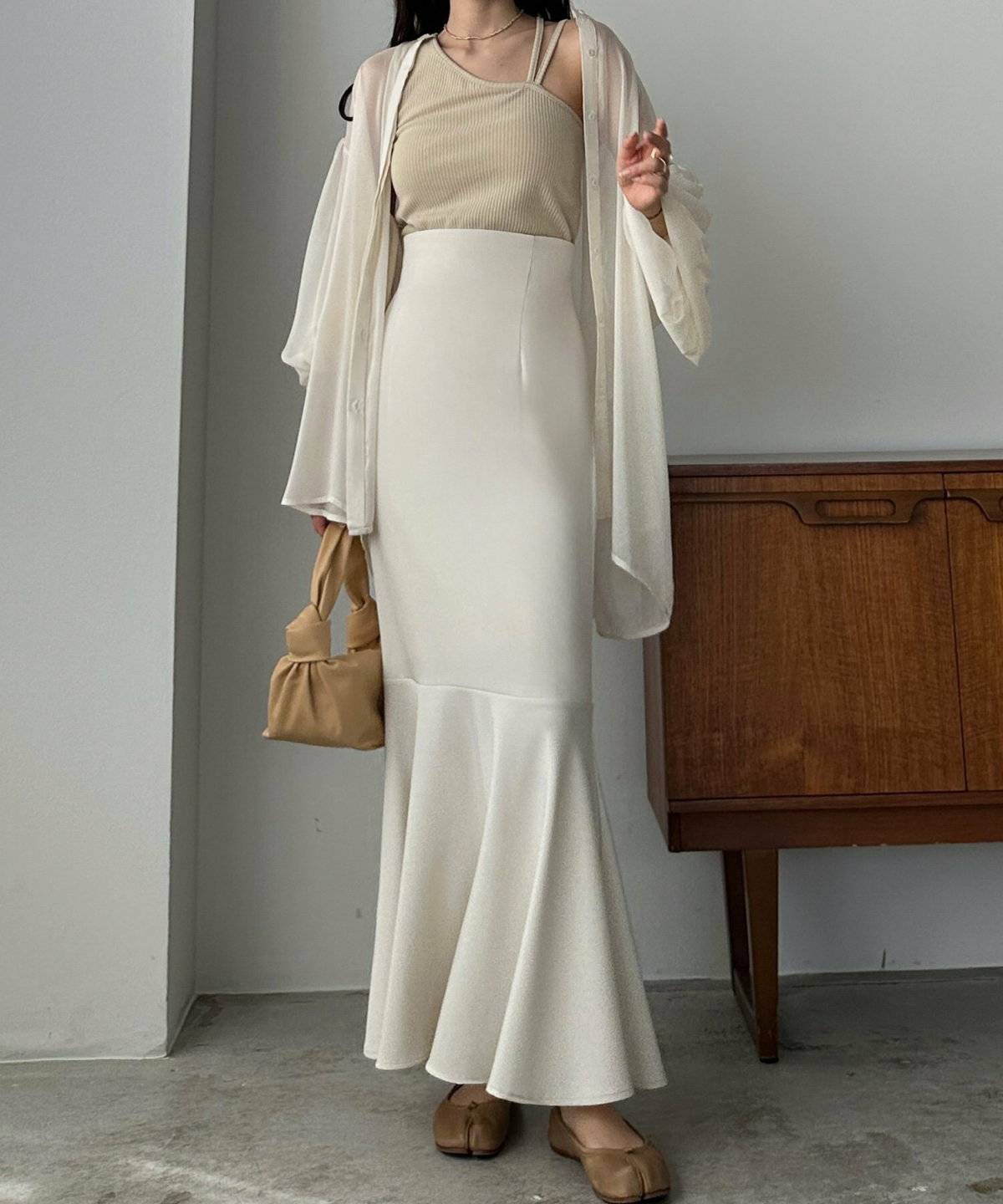 ベージュのシアーシャツに白のマーメイドスカートを合わせた女性