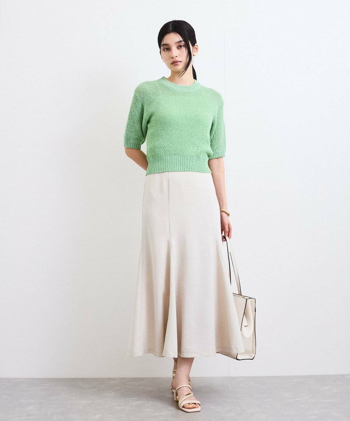 グリーンのニットにベージュのマーメイドスカートを合わせた女性