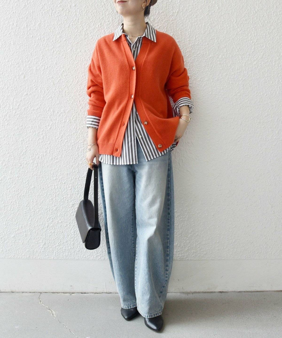 オレンジのカーディガンにデニムパンツを合わせた女性