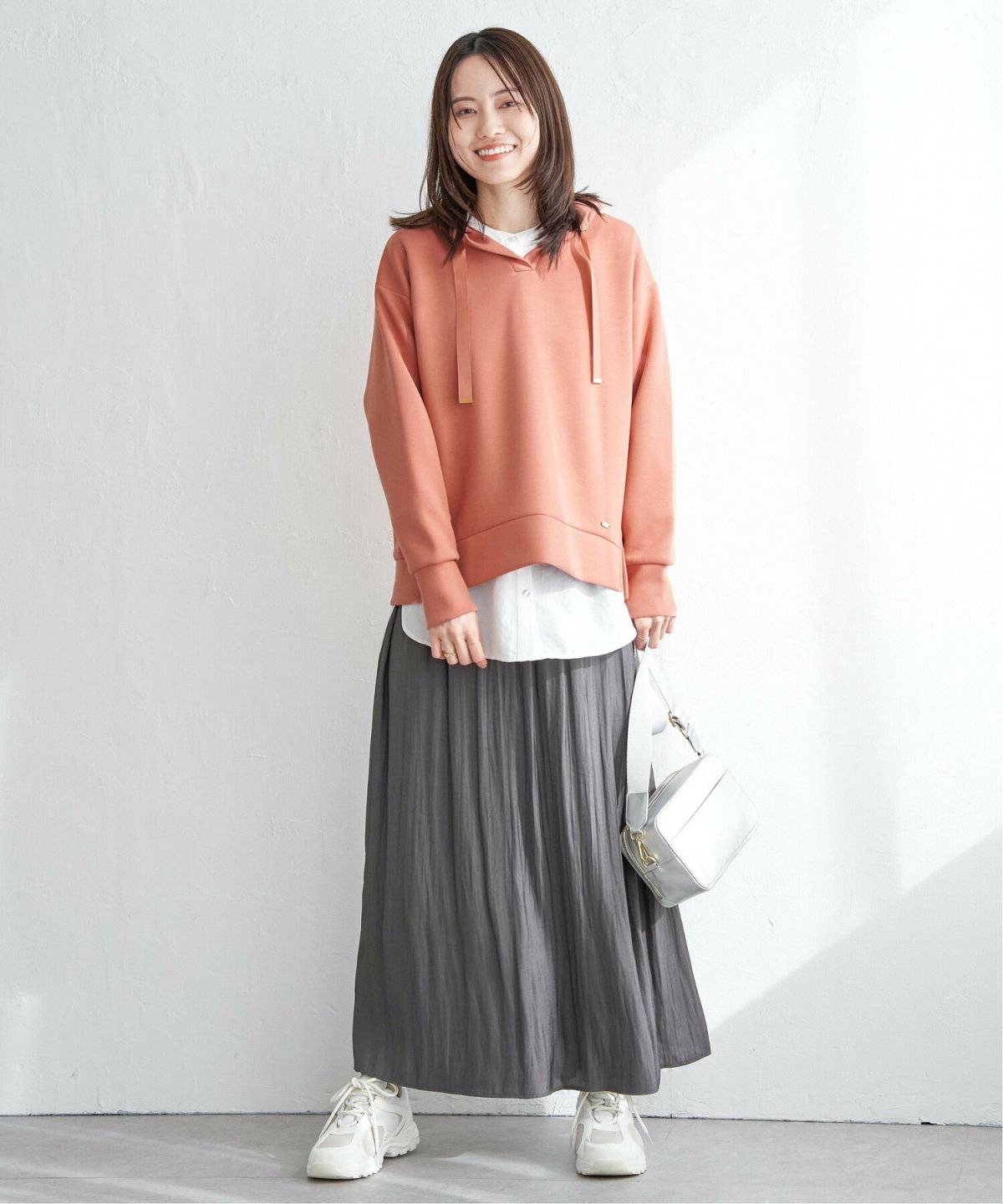オレンジのパーカーに白スカートを合わせてネイビーのコートを羽織った女性