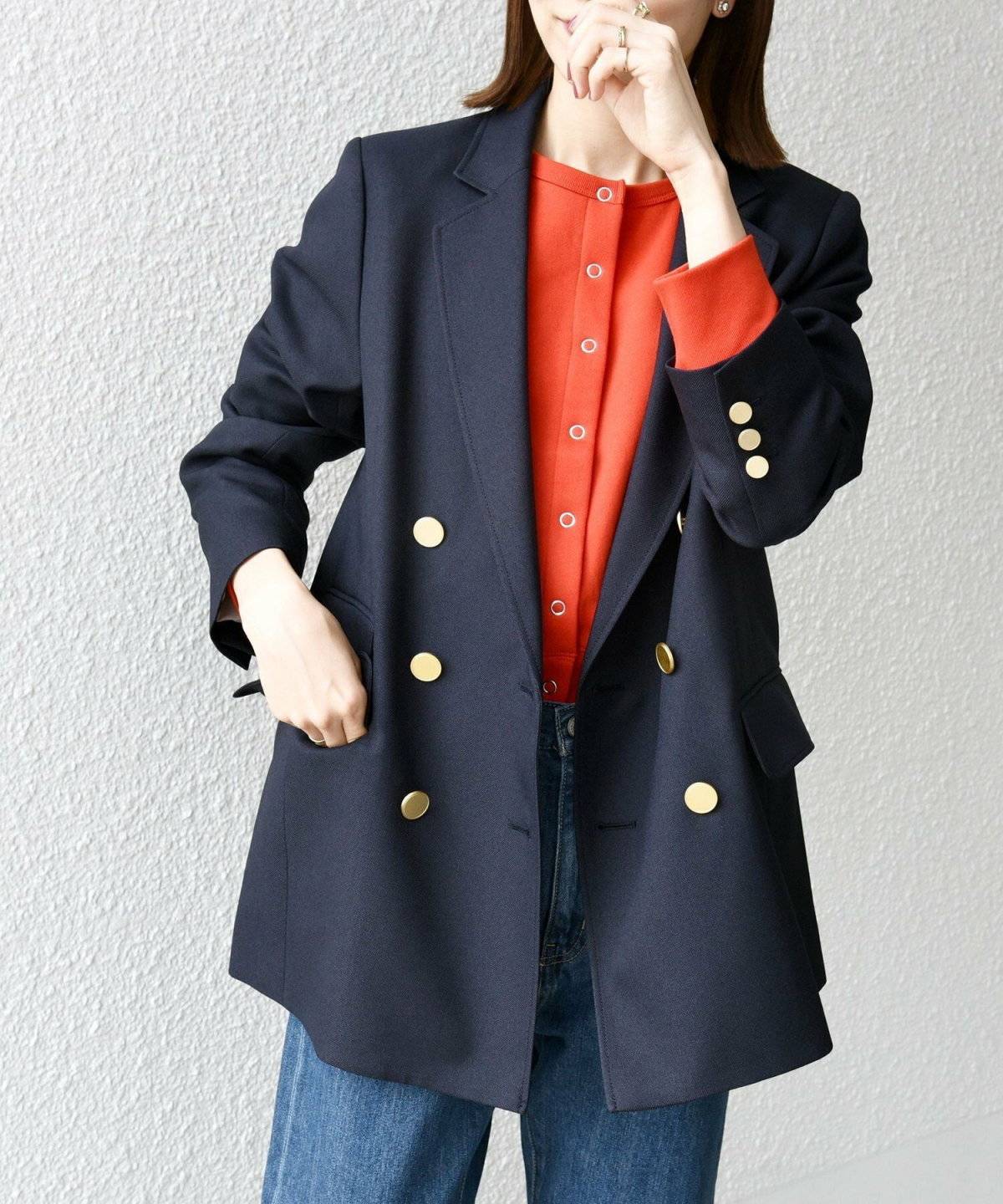 赤ニットにネイビーのジャケットを羽織ってデニムを穿いた女性