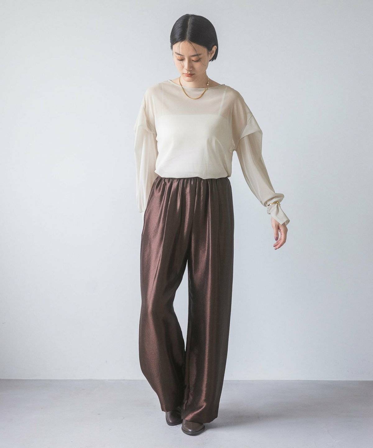 ベージュのトップスにブラウンのパンツを合わせた女性
