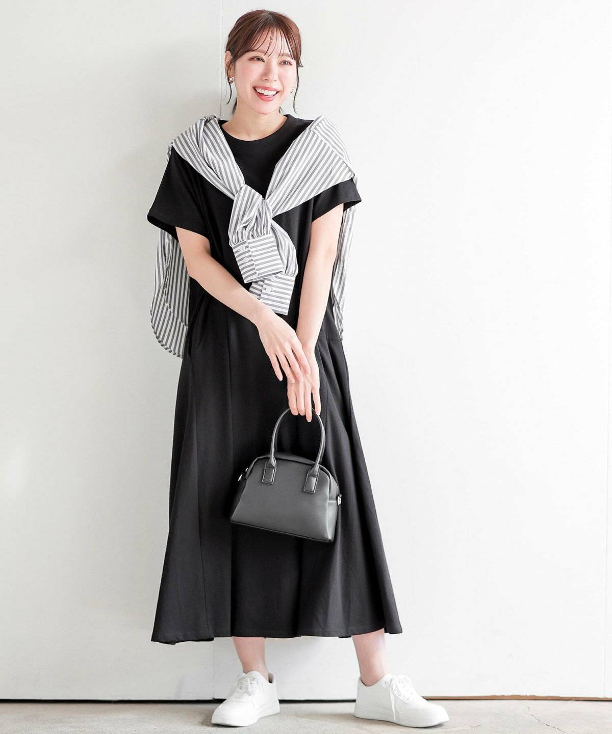 黒ワンピースにストライプ柄のシャツをたすき掛けした女性