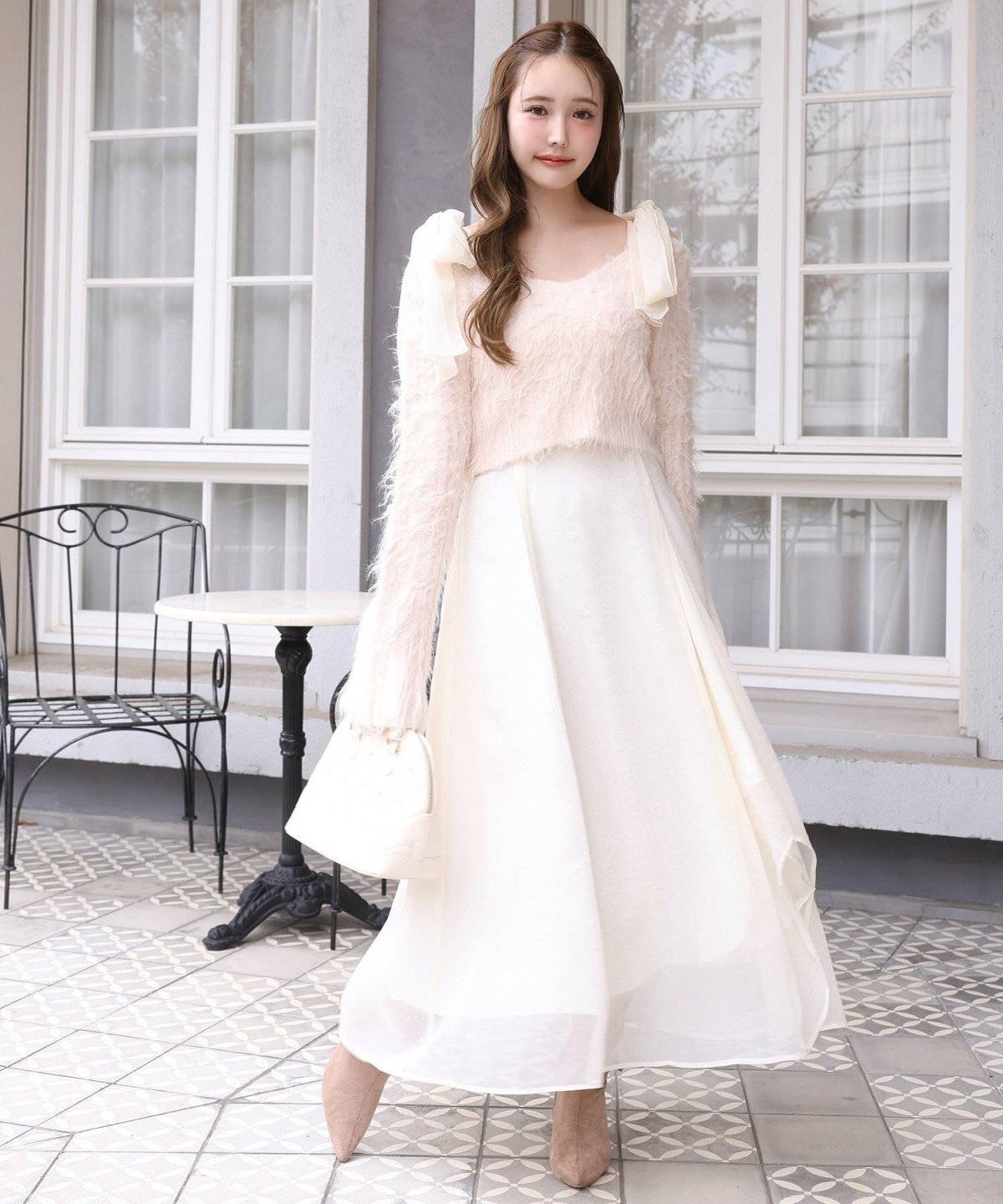 白ワンピースの上にピンクニットを重ねた女性