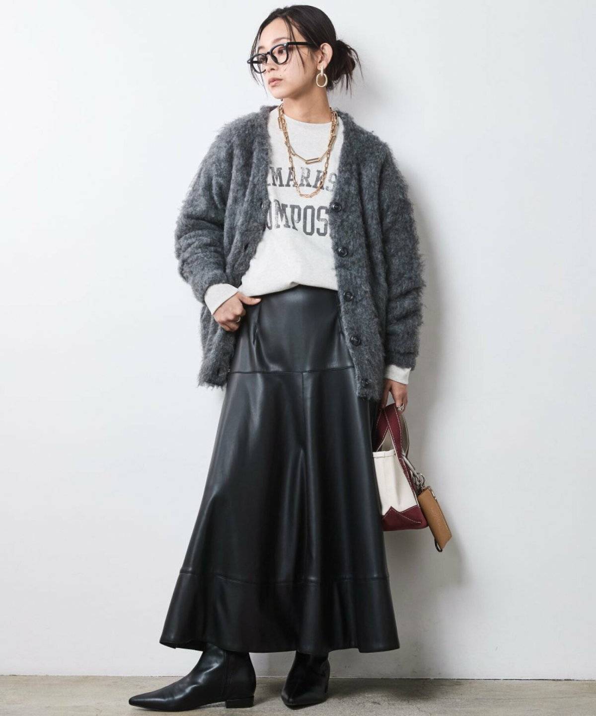 カーディガンにフェイクレザースカートを合わせた女性