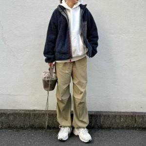  白パーカーの上に黒アウターを羽織ってベージュパンツを穿いた女性 