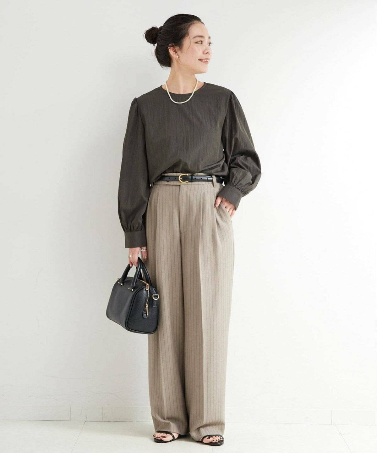黒ブラウスにベージュのパンツを合わせた女性