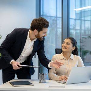  パソコンを指さしながら同僚の女性にアドバイスする男性 