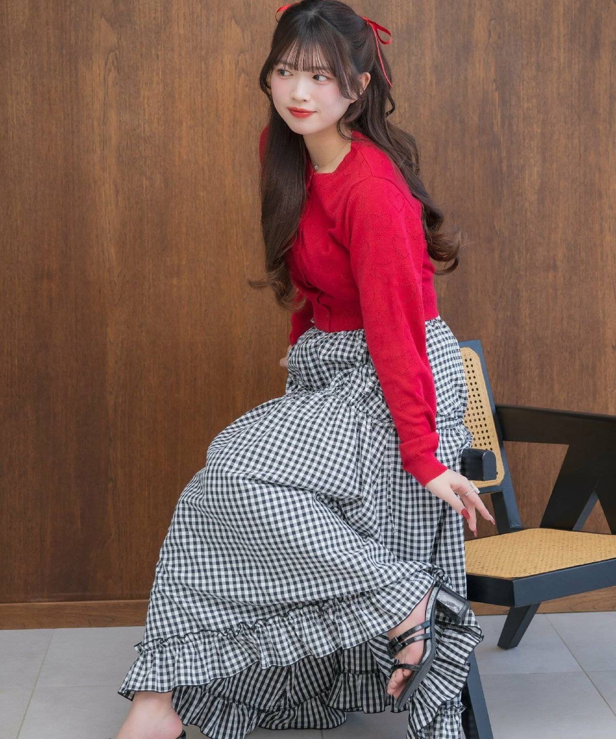 赤のカーディガンにギンガムチェック柄のスカートを合わせた女性