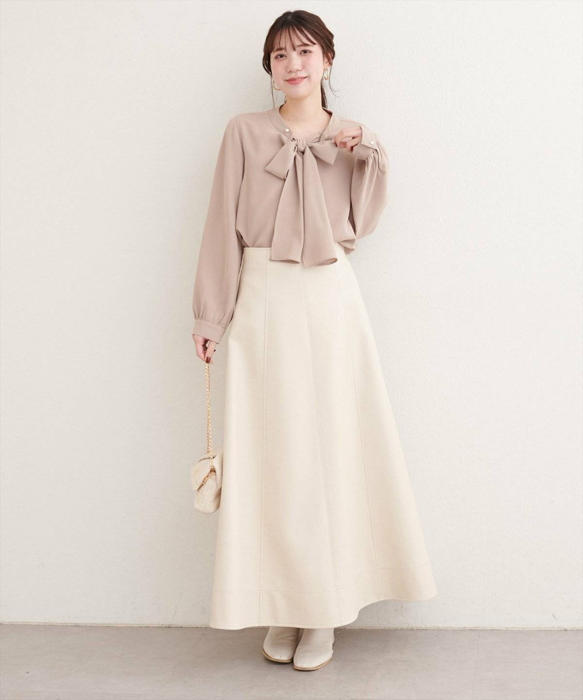 ベージュのブラウスに白のスカートを合わせた女性