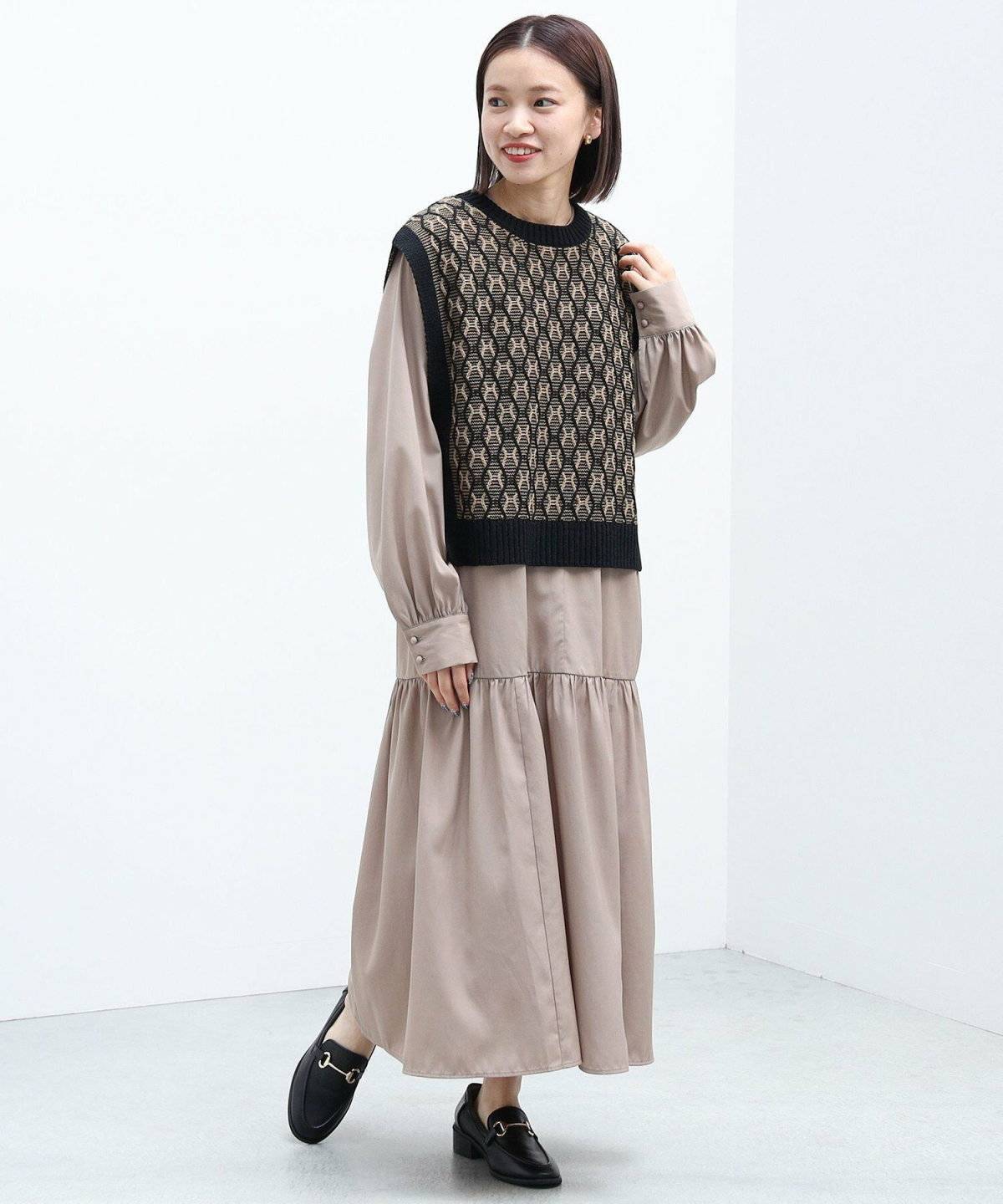 ベージュのワンピースに黒のベストを重ねた女性