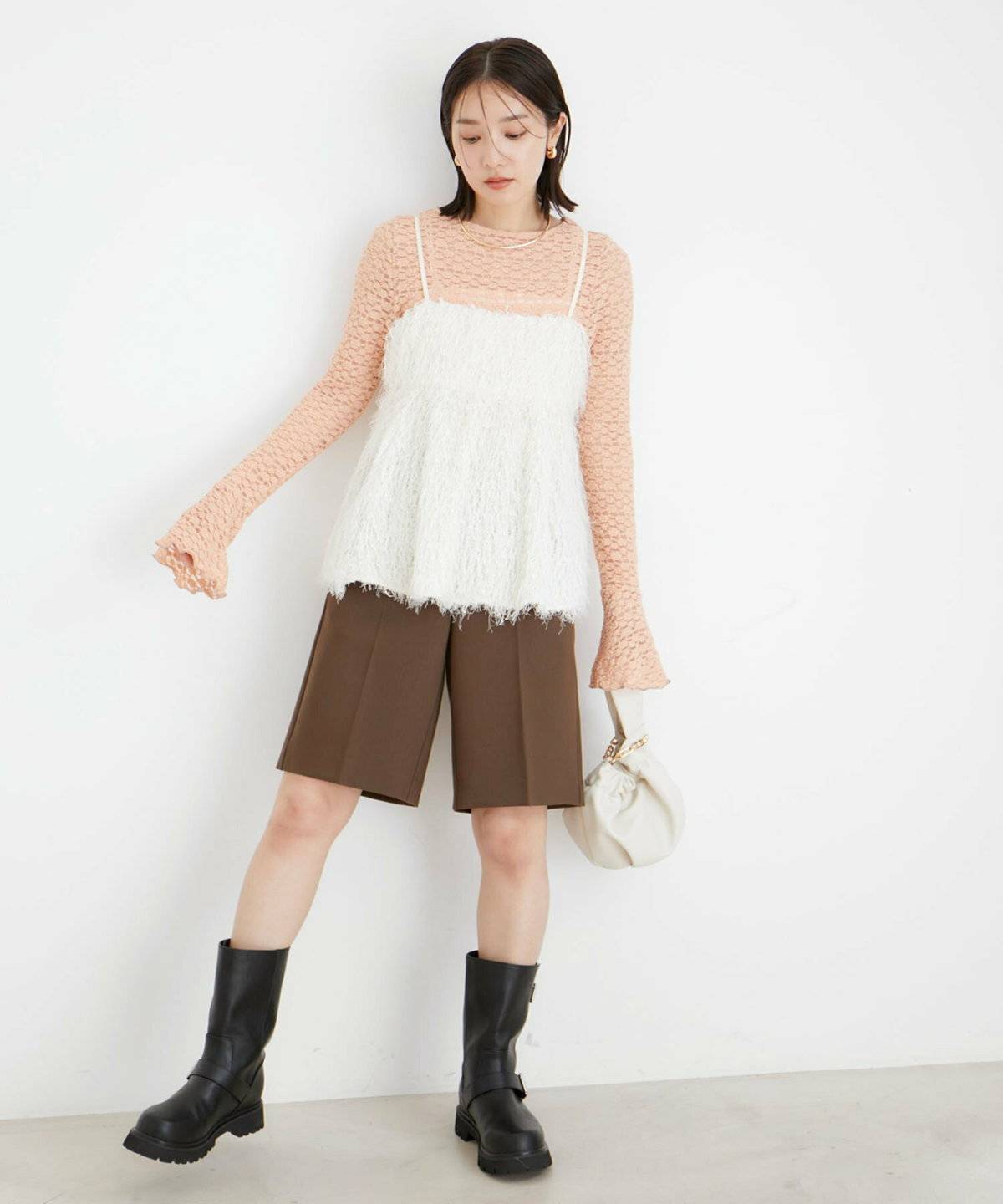 ピンクのトップスに白のキャミソールを重ねてパンツを合わせた女性