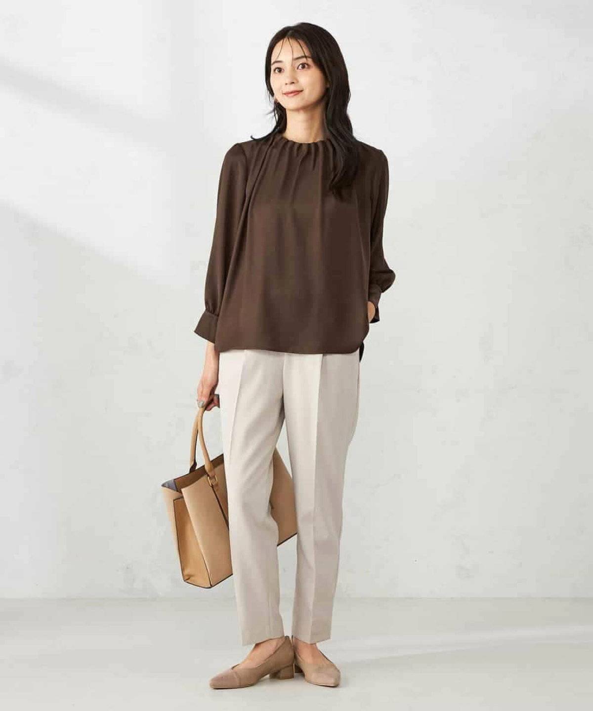 ブラウンの長袖ブラウスにベージュのパンツを合わせた女性