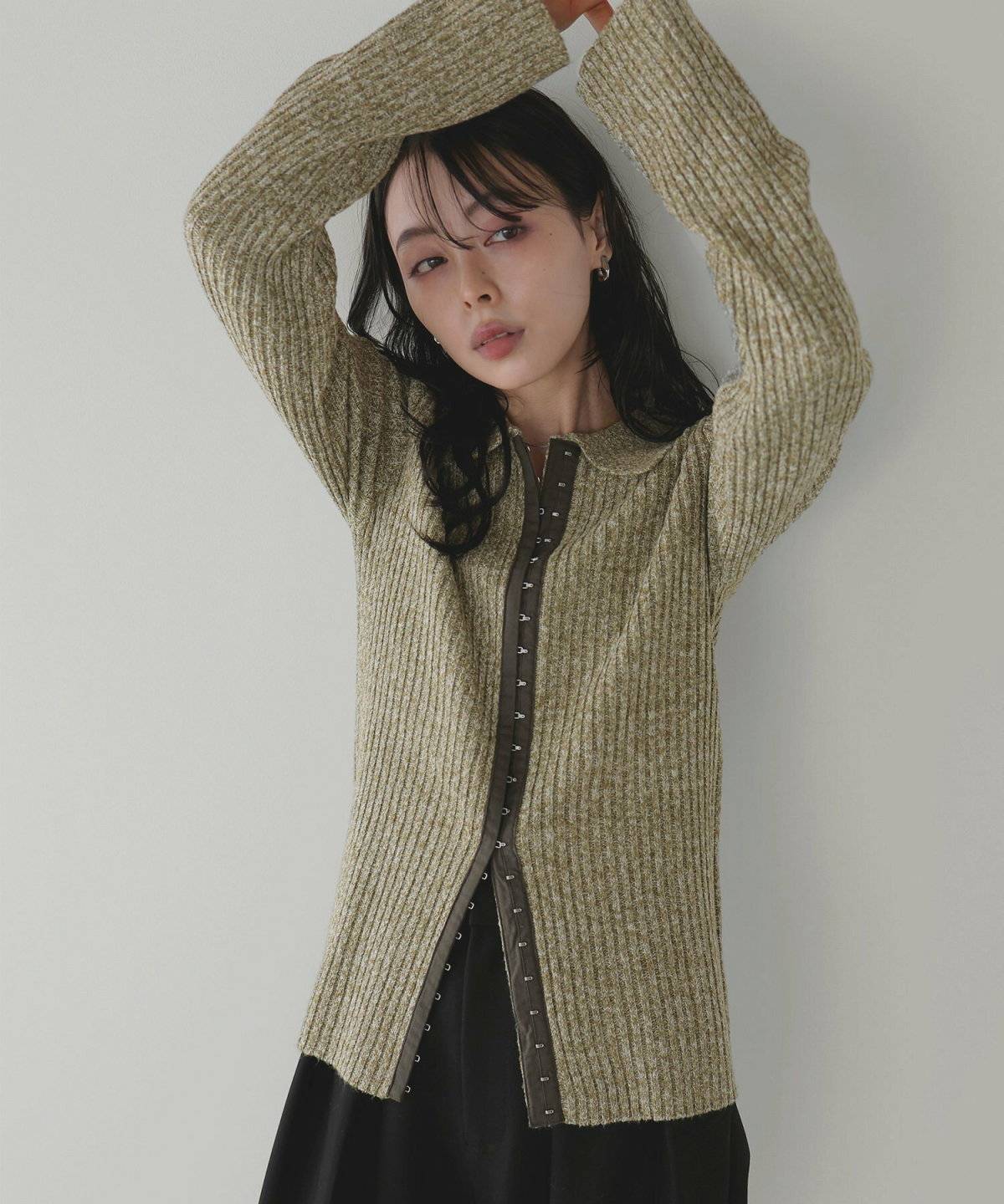 黒ワンピースにグリーンのプルオーバーを重ねた女性