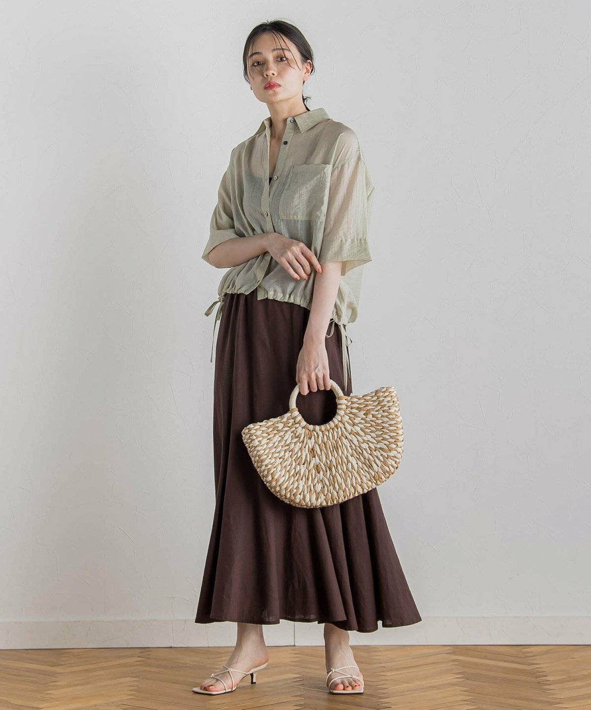 グリーンのシアーシャツにブラウンのスカートを合わせた女性