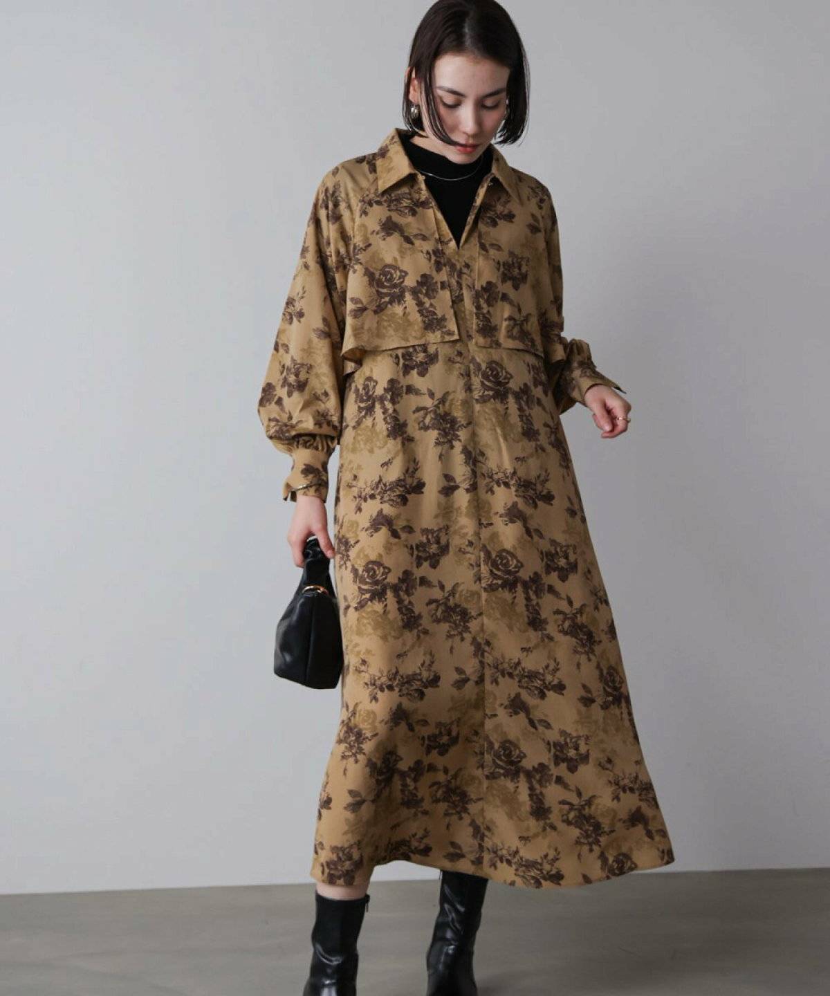 黒のハイネックにベージュのワンピースを重ねて白カーディガンを肩掛けした女性