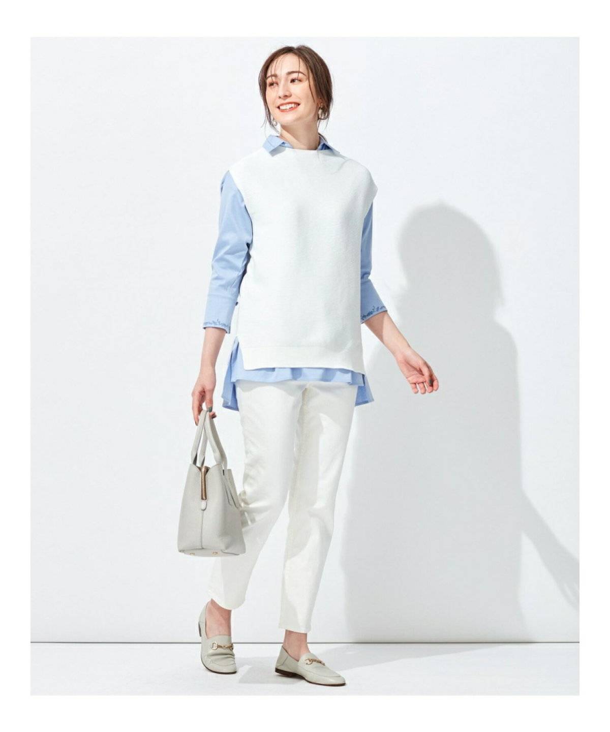 シャツにベージュのベストを重ねて白パンツを合わせた女性