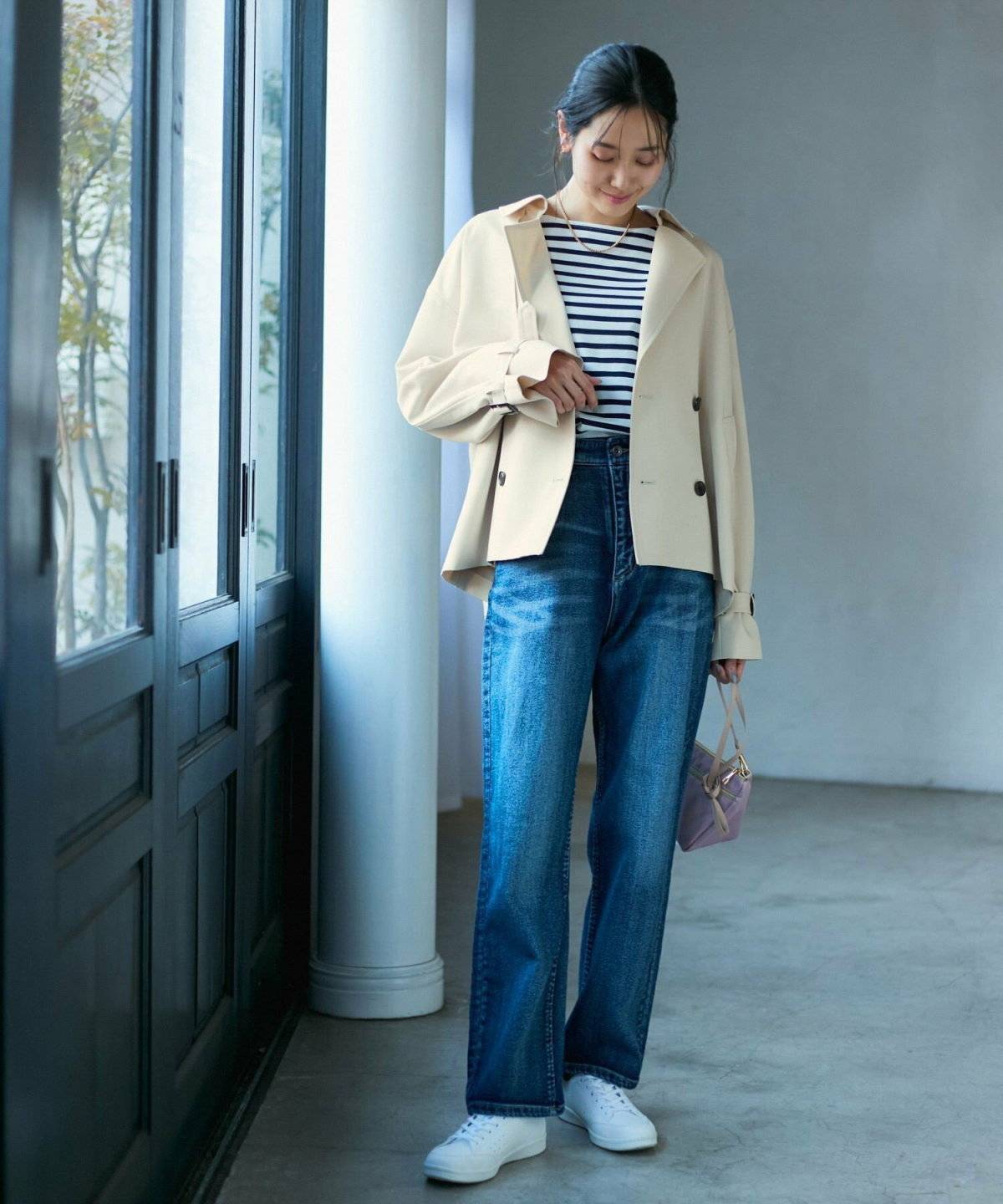 ボーダー柄のカーディガンにデニムを合わせてトレンチコートを羽織った女性