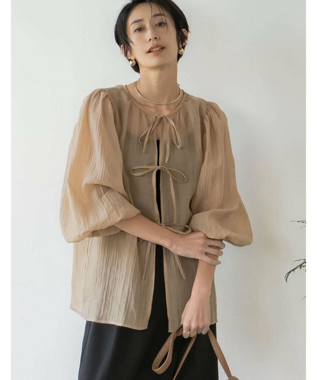 黒ワンピースにベージュのブラウスを重ねた女性