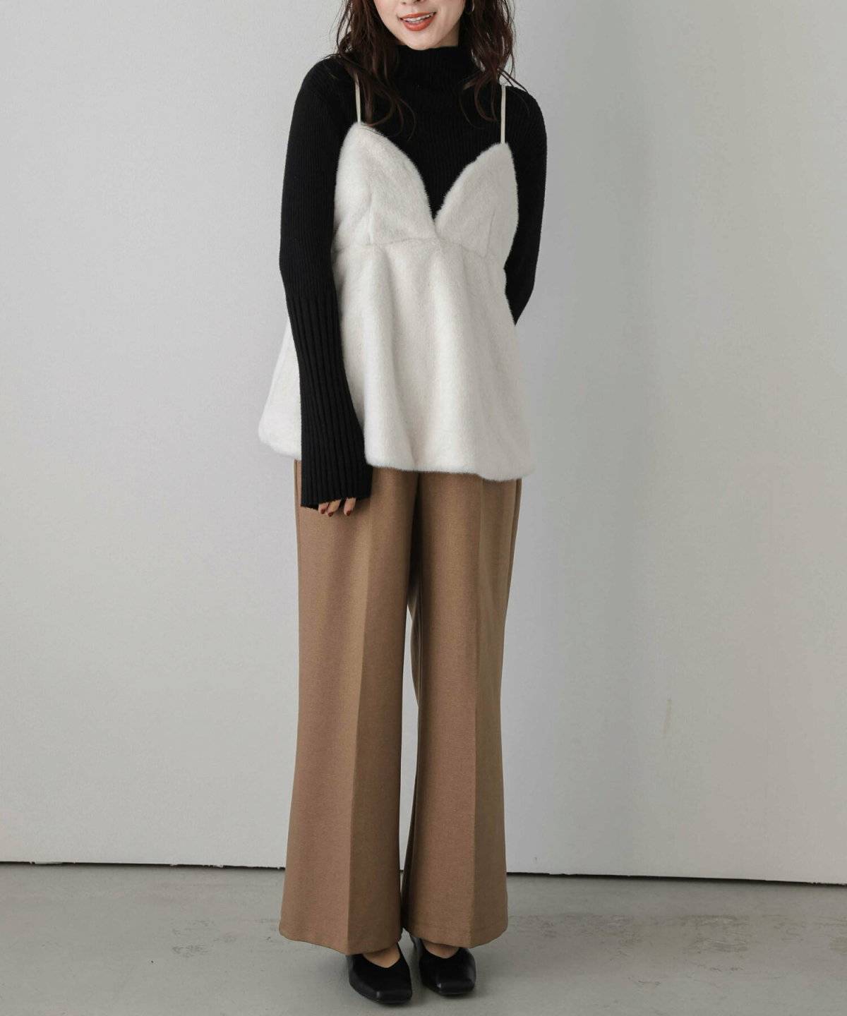 白ニットに黒キャミソールを重ねてベージュのパンツを合わせた女性