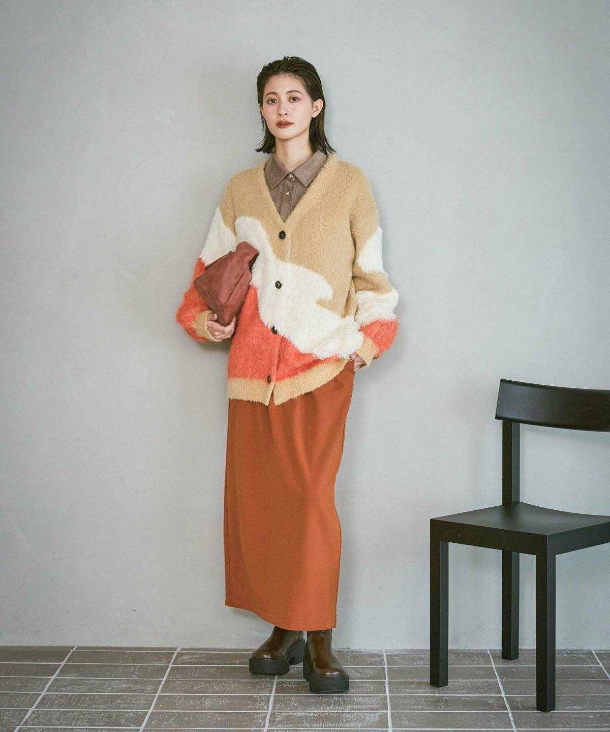 オレンジのカーディガンにブラウンのスカートを合わせた女性