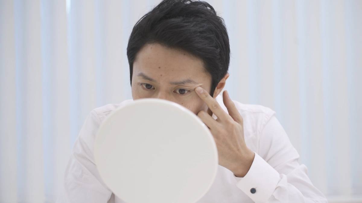 手鏡で自分の顔を見る男性