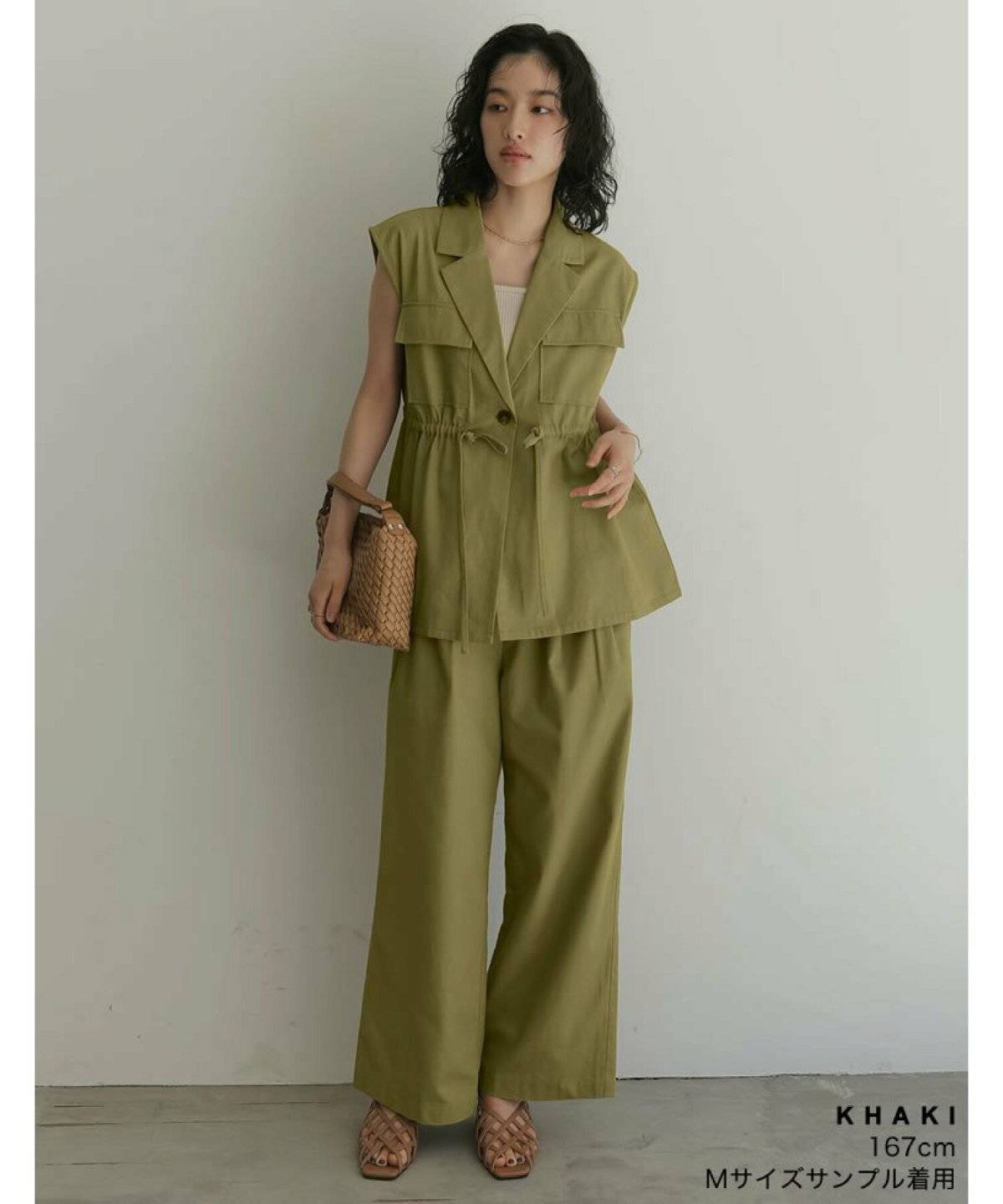 カーキのベストに黒パンツを合わせた女性