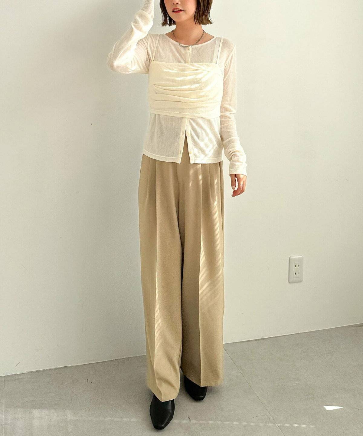 白トップスにベージュのチュールビスチェを重ねてベージュパンツを合わせた女性