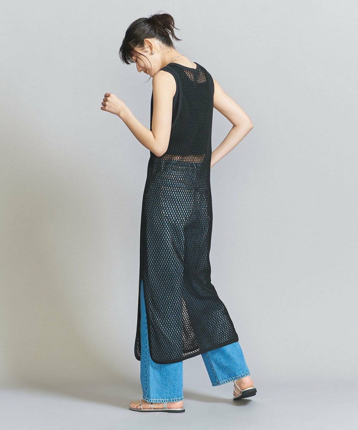 グリーンのブラウスに黒パンツを合わせて黒ワンピースを重ねた女性