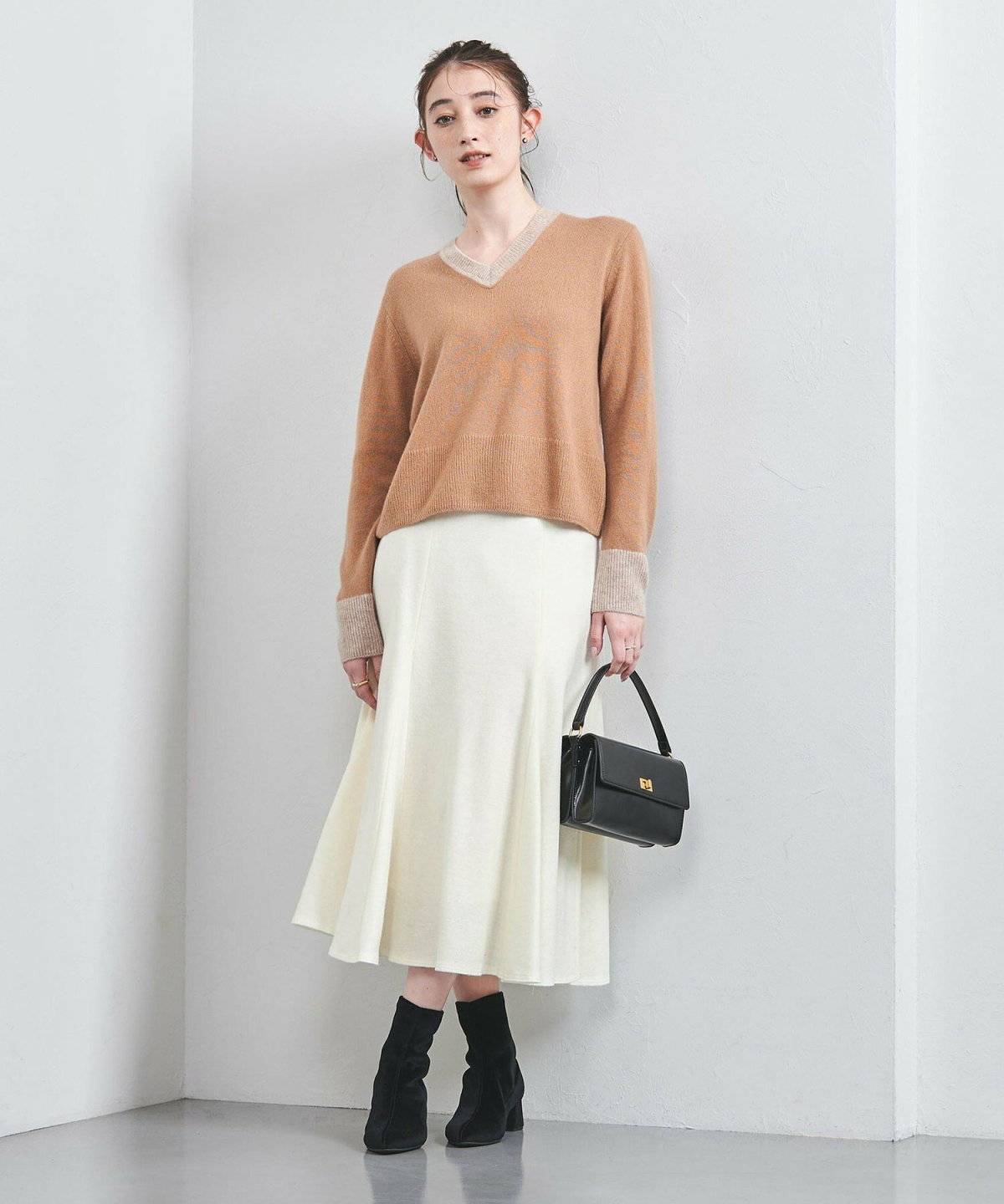 ベージュのニットに白スカートを合わせた女性