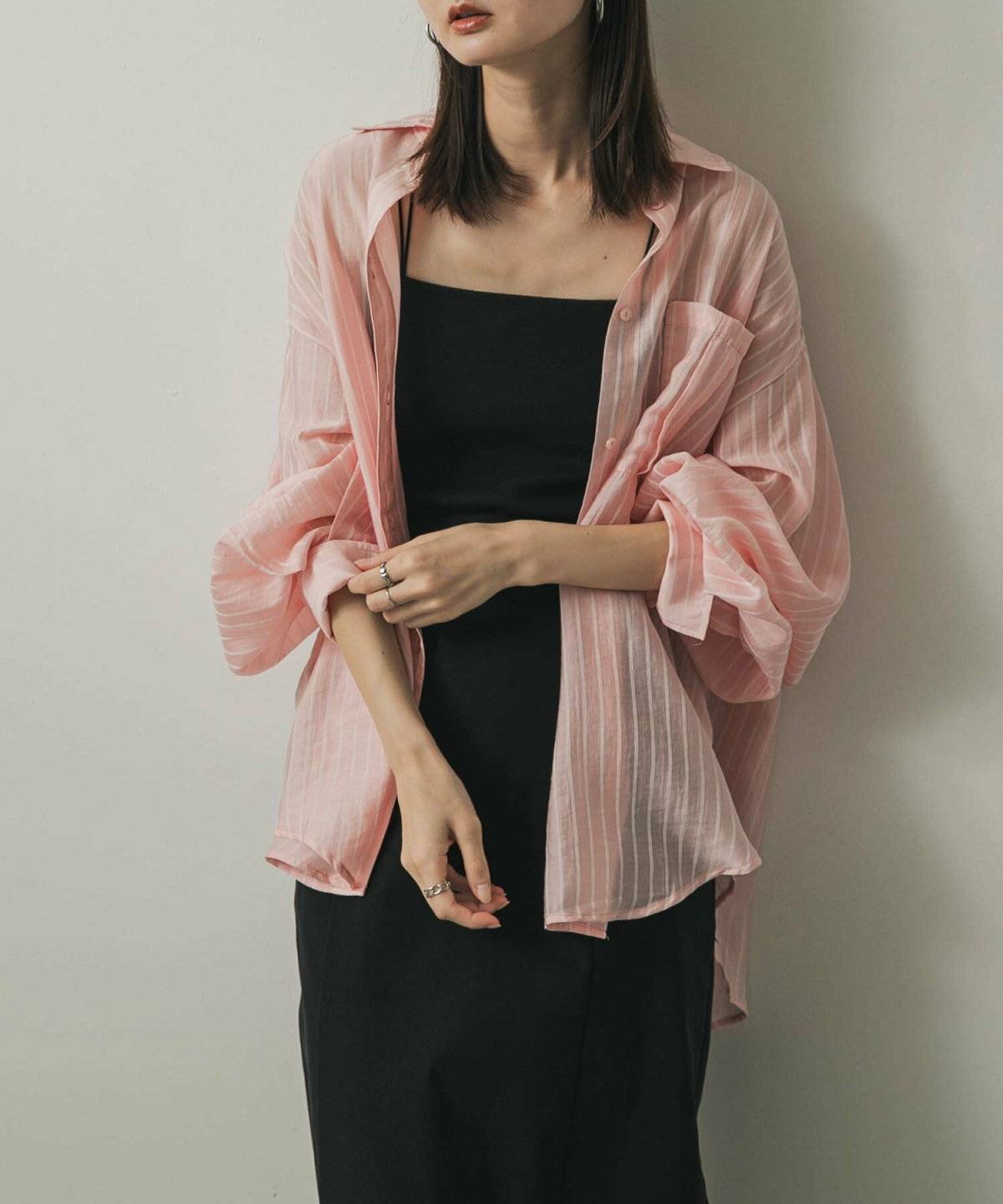 黒ワンピースにピンクのシャツを羽織った女性