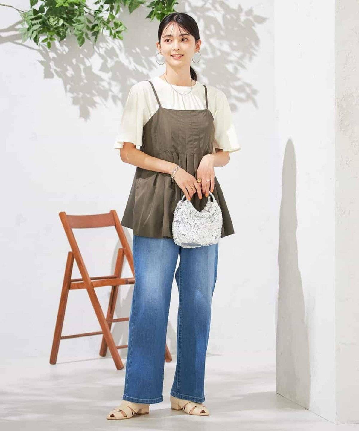 ベージュのカットソーにグリーンのキャミを重ねて黒パンツを合わせた女性